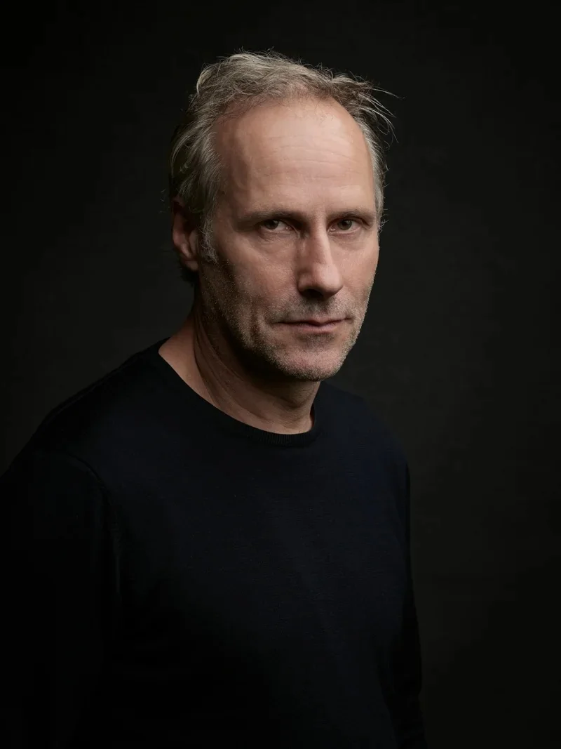 Close-up portrait of a man with greying hair and intense eyes against a dark background.